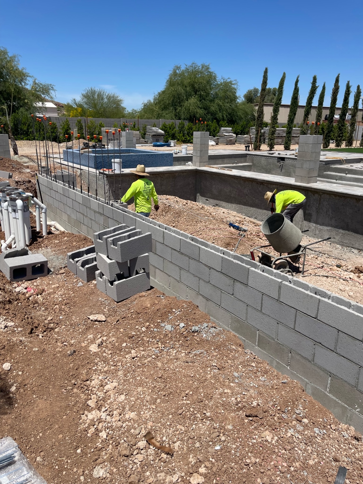 Aurora Estate — masonry crew building the long block wall beside the pool structure during the hardscape phase