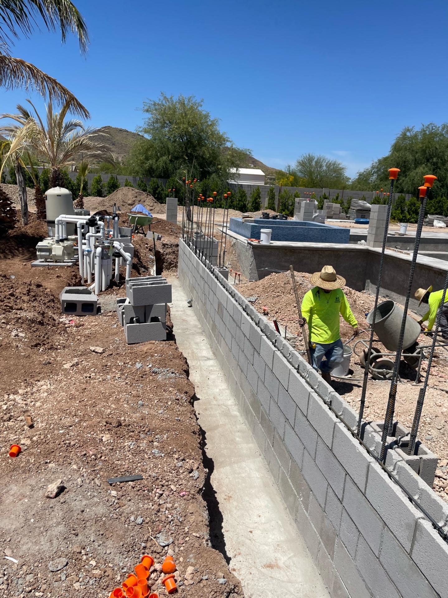 Aurora Estate — long block wall under construction with the pool equipment skid, plumbing manifold, and desert mountain backdrop visible beyond