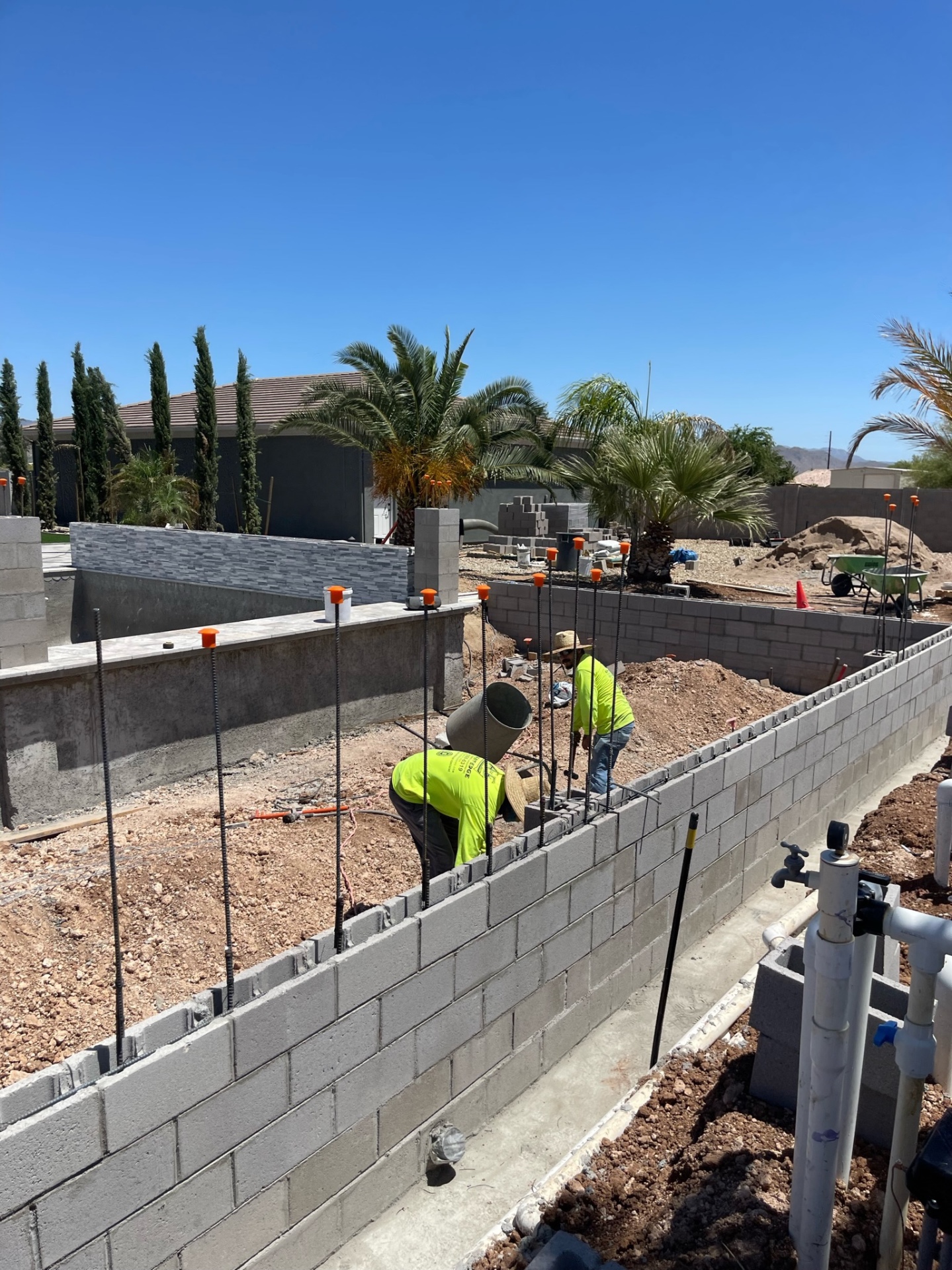 Aurora Estate — close masonry view of the long block wall as the crew fills cells and builds out the run beside the pool and raised spa walls