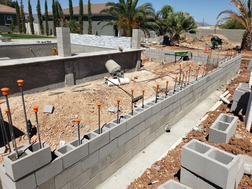 Aurora Estate — long block wall rising along the property line with the spa shell and glass tile waterline visible in the background