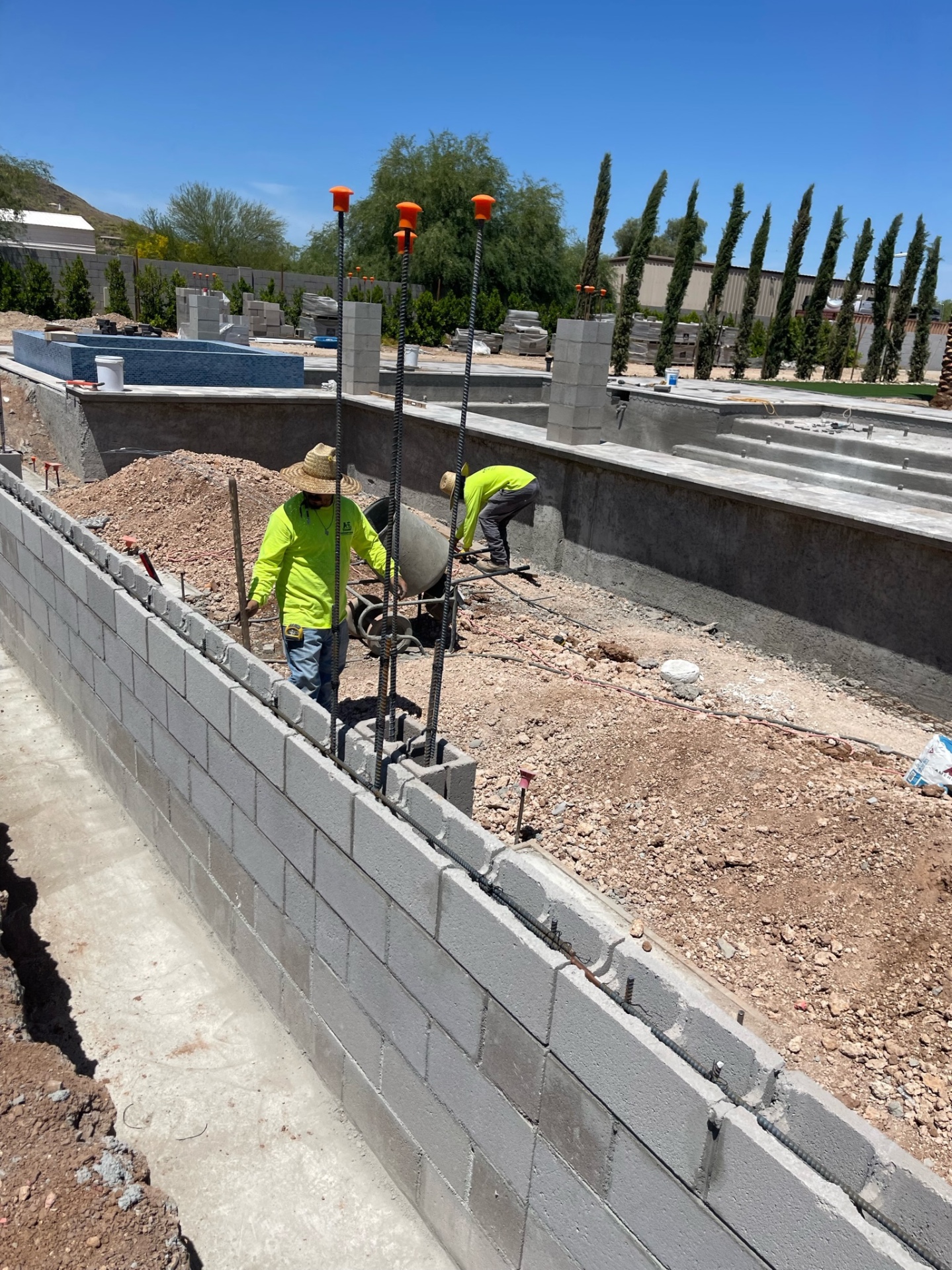 Aurora Estate — masonry crew wet-setting and filling the long block wall beside the pool shell with rebar columns rising above the wall line