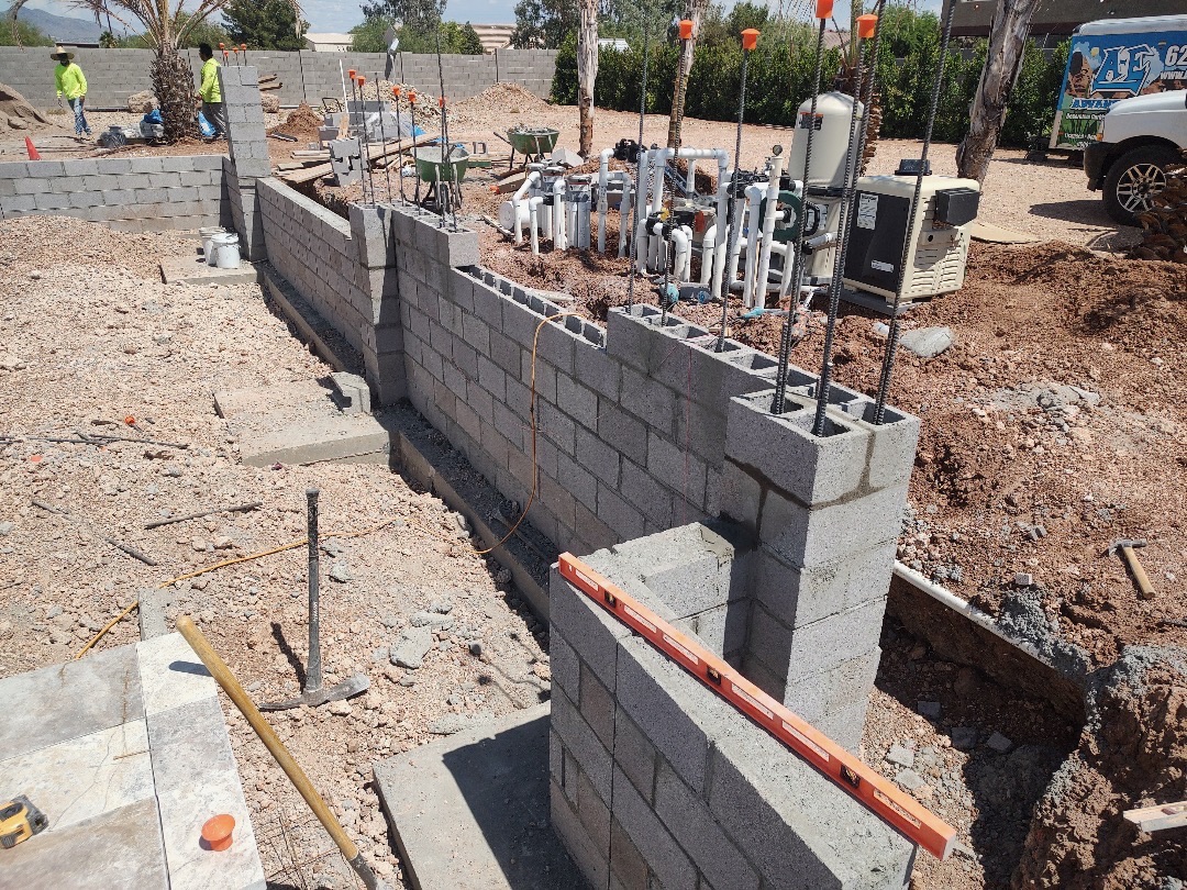 Aurora Estate — equipment pad with manifold of pool plumbing, valves, heater, and pump system behind a block screen wall before backfill and stucco