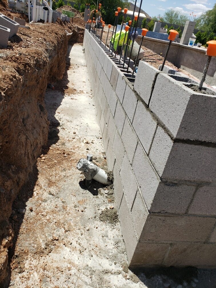 Aurora Estate — narrow footing trench against the new block wall showing concrete pour, plumbing stub, and reinforcement