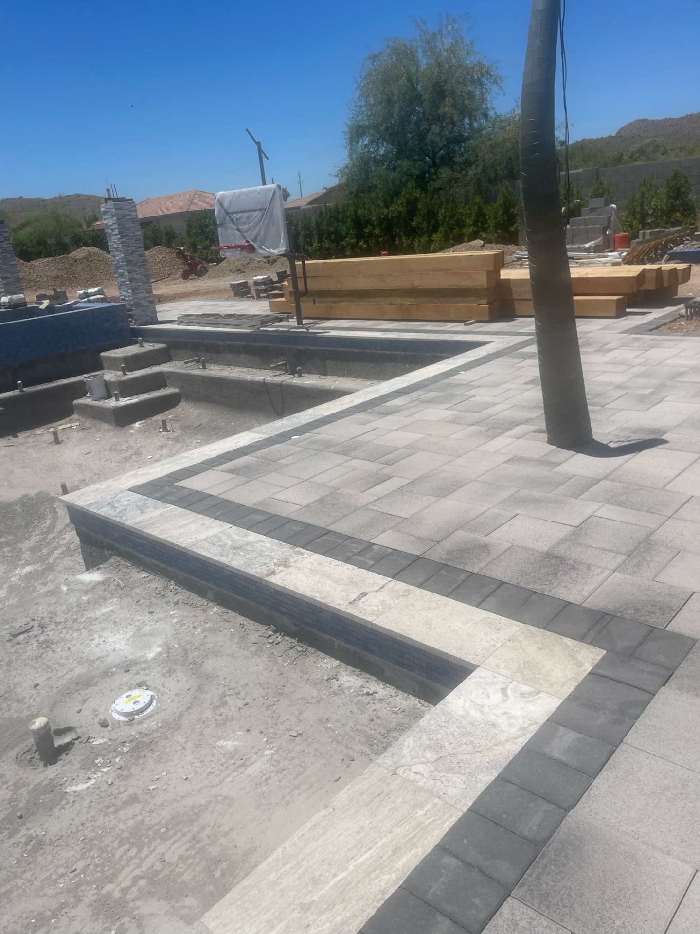 Aurora Estate — paver corner with charcoal and travertine banding detail beside the planter wall, with ramada timbers staged in the background