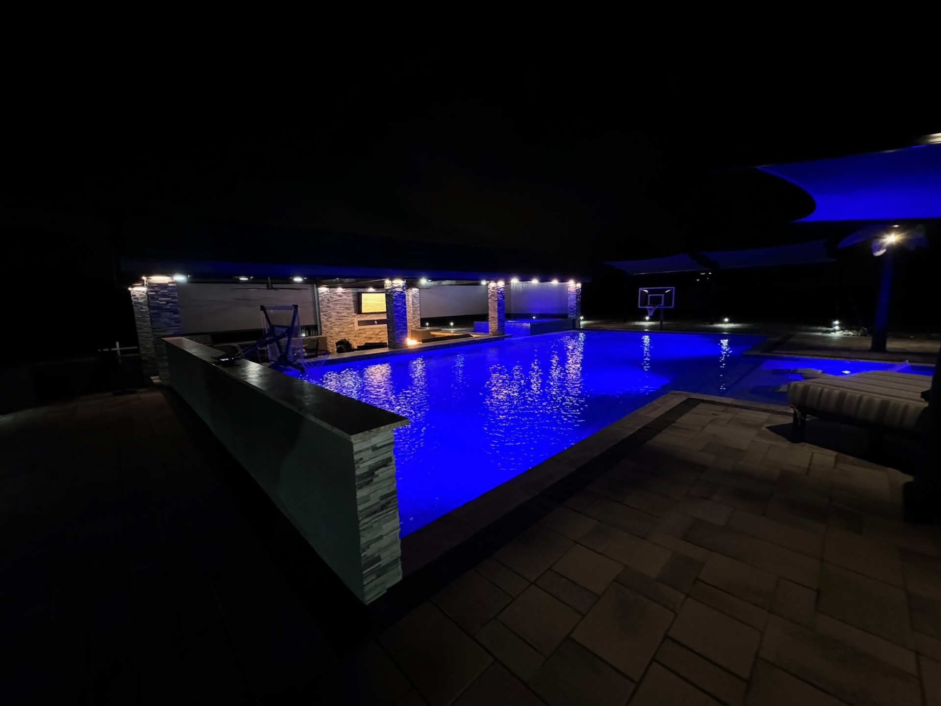 Aurora Estate — vanishing edge pool at night with shade sail and basketball court
