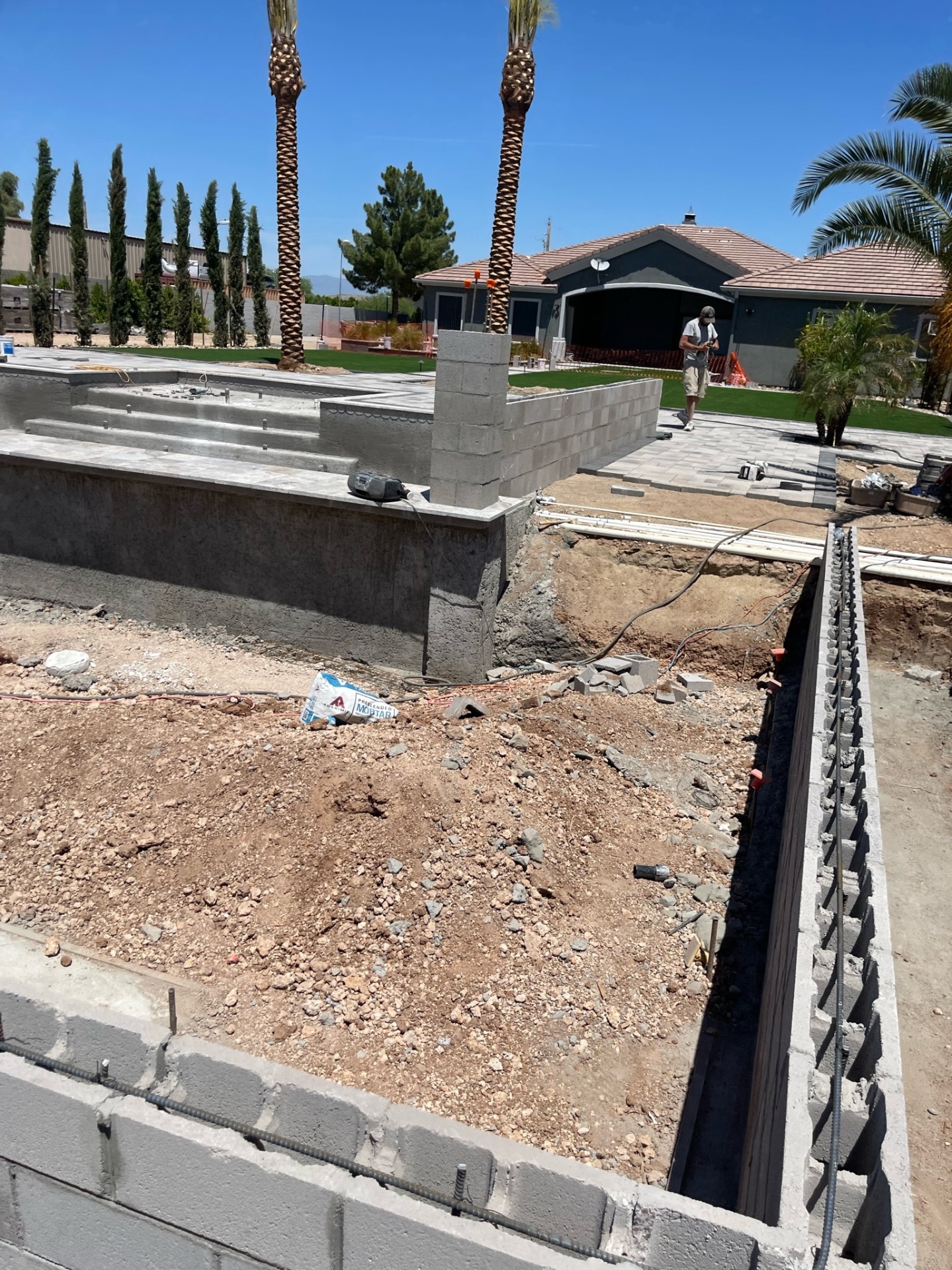 Aurora Estate — wide overview of the empty pool shell, raised wall sections, new masonry runs, and deck field forming around the main pool