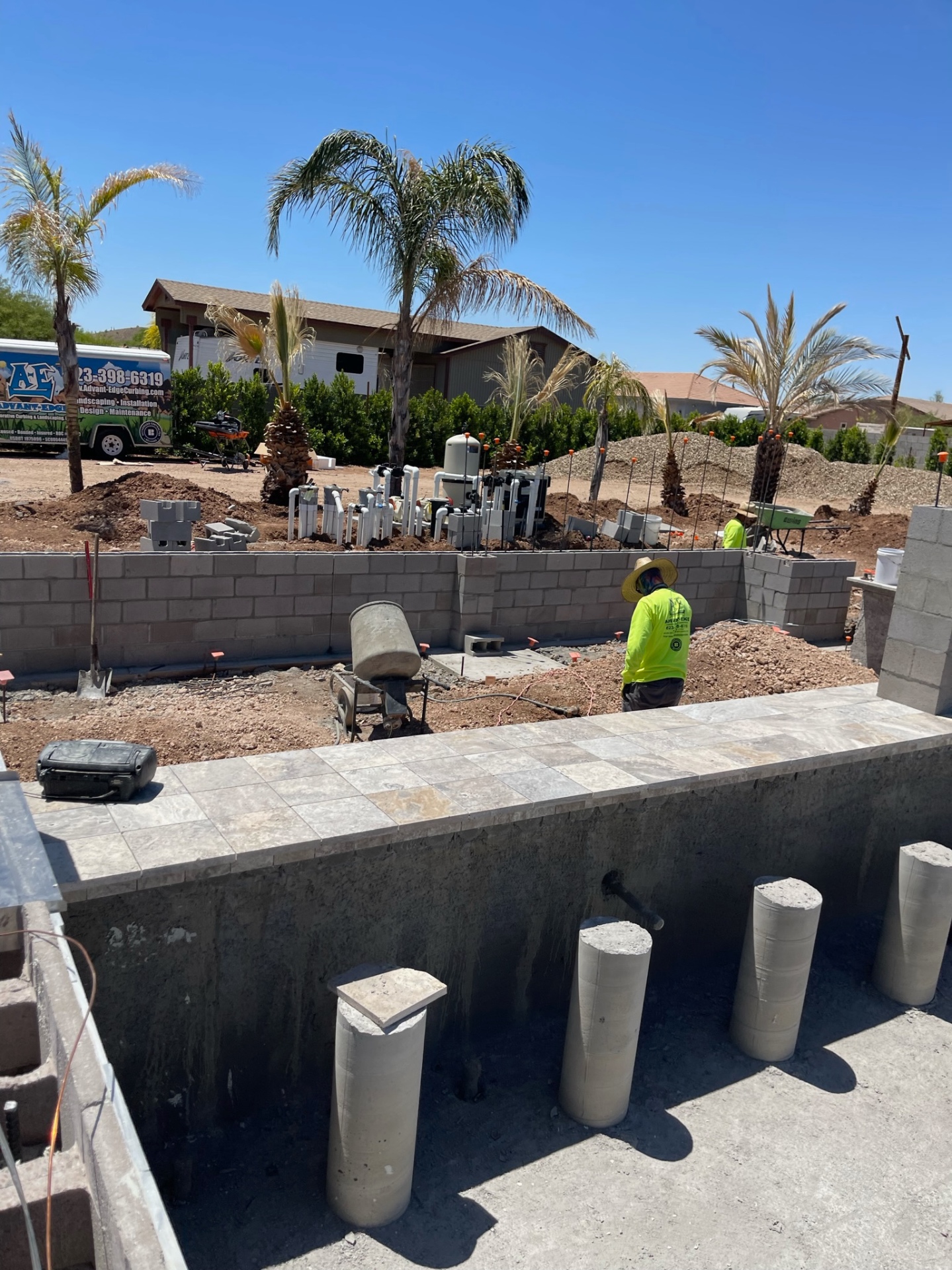 Aurora Estate — view from inside the empty pool shell toward the equipment wall, masonry runs, and palms as structural systems converge