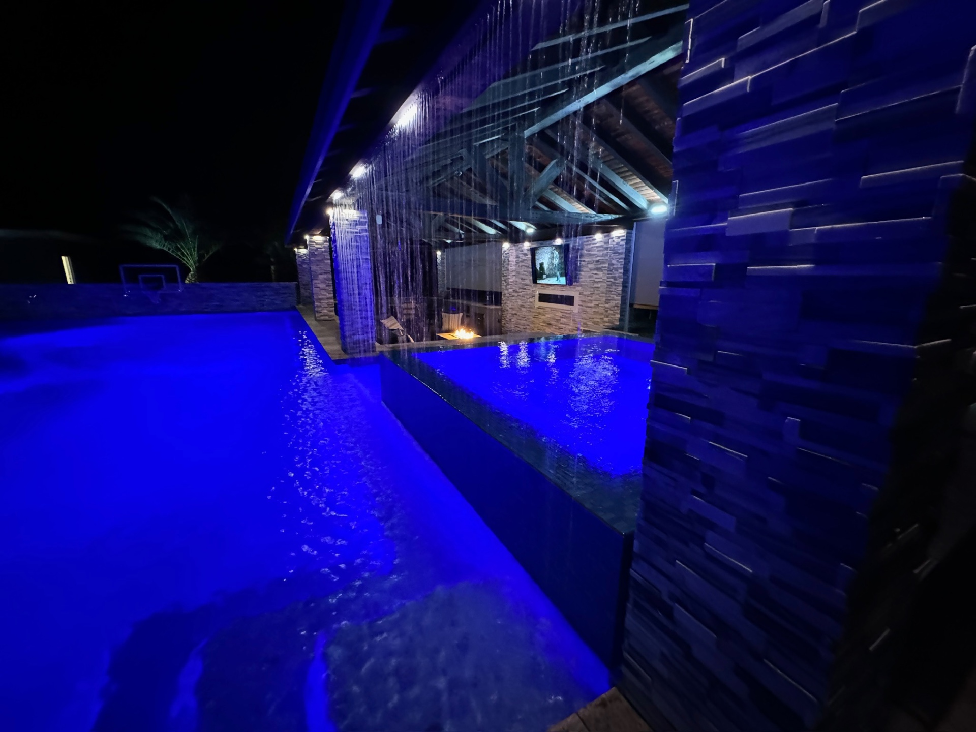 Aurora Estate — rain curtain backlit in deep cobalt with stacked-stone columns