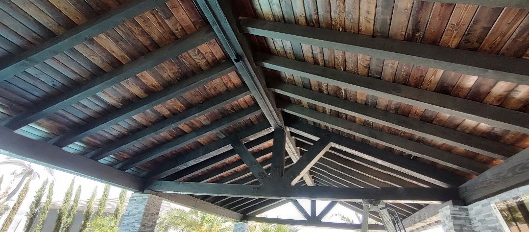 Aurora Estate — stained tongue-and-groove ramada ceiling with exposed black steel rafters and trusses