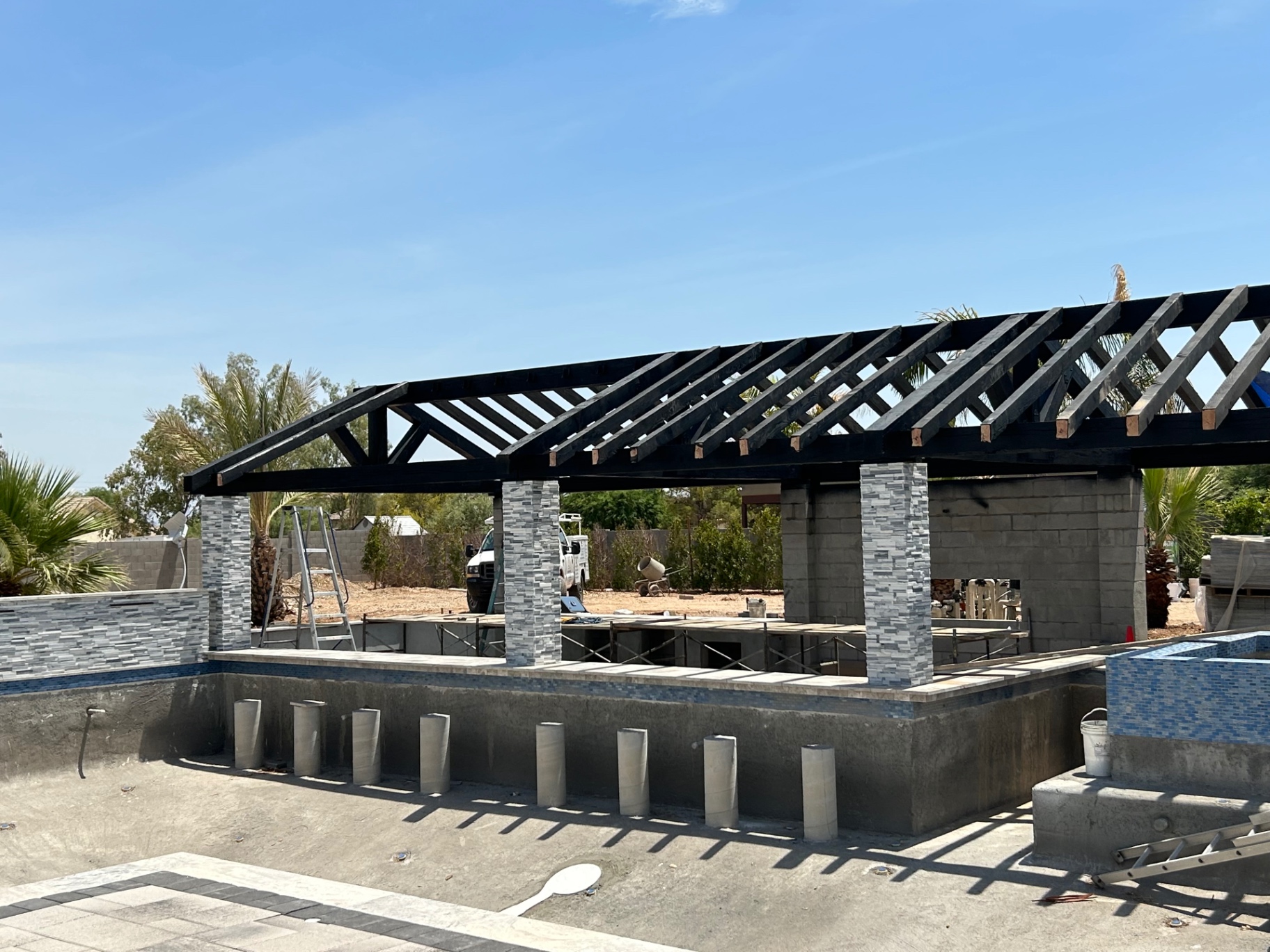 Aurora Estate — ramada framing and stacked-stone column work above the empty pool shell