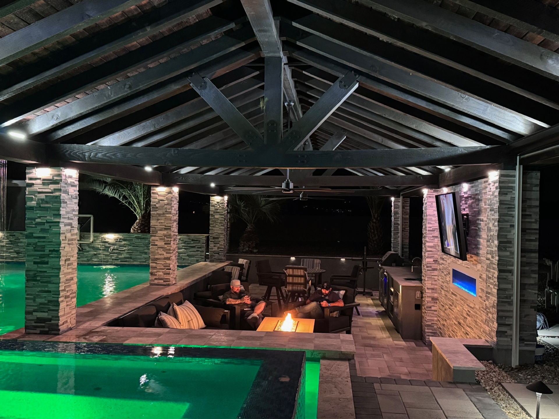 Aurora Estate — gabled cedar ramada interior with exposed trusses, ceiling fan and outdoor TV