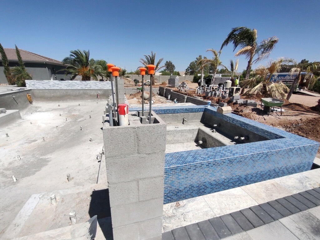 Aurora Estate — close-up of the blue mosaic glass tile on the raised spa spillway with rebar columns rising for the ramada