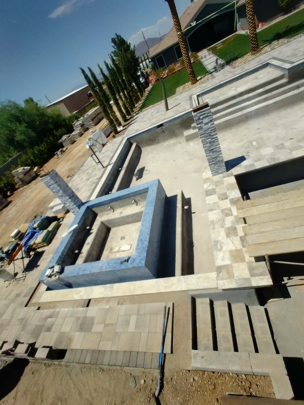 Aurora Estate — overhead view of the raised spa wrapped in blue mosaic glass tile with travertine deck banding and stacked-stone columns