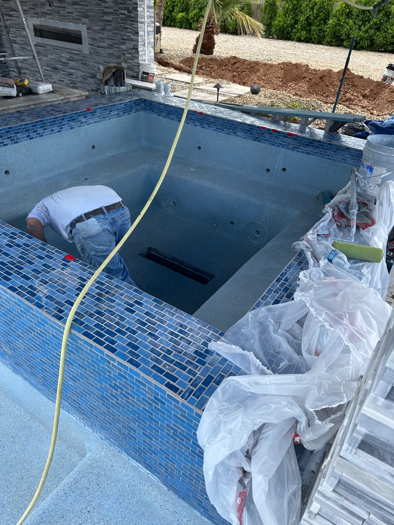 Aurora Estate — raised spa with mixed blue glass-tile waterline and pebble interior nearing completion