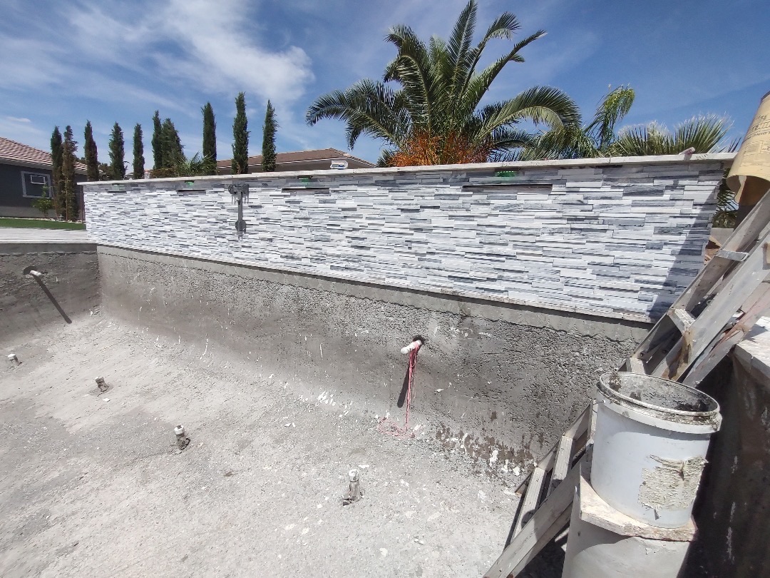 Aurora Estate — raised spa wall clad in white stacked-stone with travertine cap and recessed LED light niches before water fill