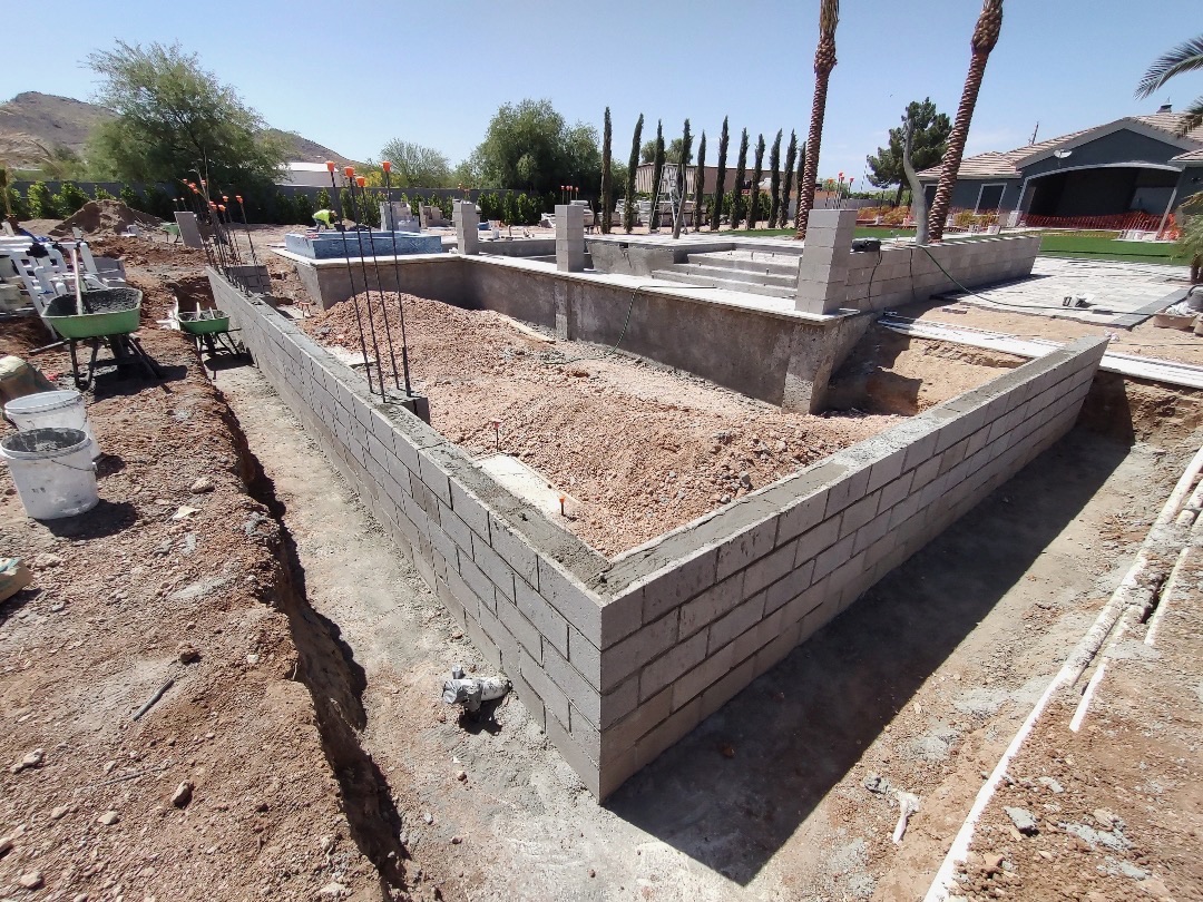 Aurora Estate — sunken lounge and pool shell in plastered block with raised spa, deck steps, and perimeter wall framing the build